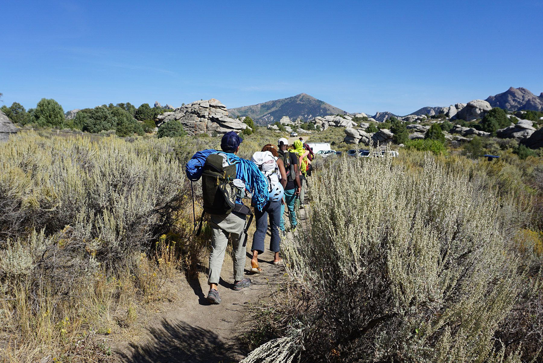 The group hikes through sage brush with packs on