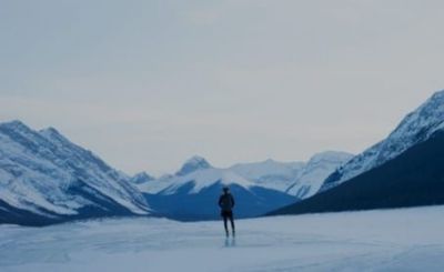 solitary figure stands among snow and ice with snow-capped mountains on the horizon