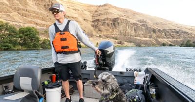 Curits Ciszek and a dog are riding on a boat out on the water.