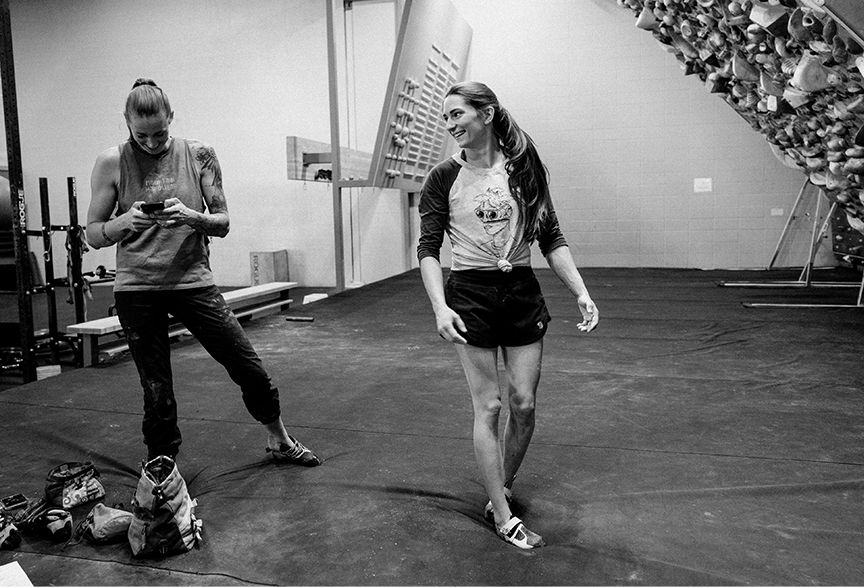 Black and white image of Alex and Kyra standing and talking in the gym