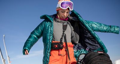 Skiier warming up, pulling on her Women's Phantom™ Down Parkaover.