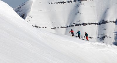 Three skiers in the distance doing a hike-to in a ski resort.