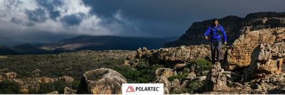 Polartec logo overlayed on a on an image of a climber on his approach in the desert. 