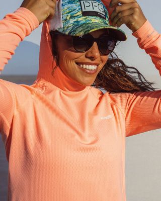 A smiling woman in a sun hoodie, sunglasses, and ballcap.